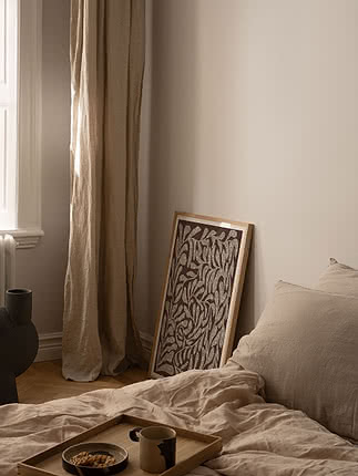 Trykket Textured Botanical i egeramme lænet op ad en beige soveværelsesvæg ved siden af hørsengetøj og en bakke