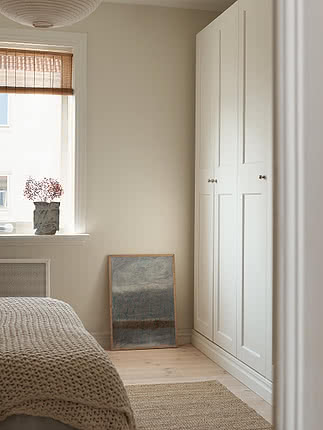 Tirage Winter Landscape dans un cadre en chêne appuyé contre un mur de chambre beige près d'une fenêtre à store tissé