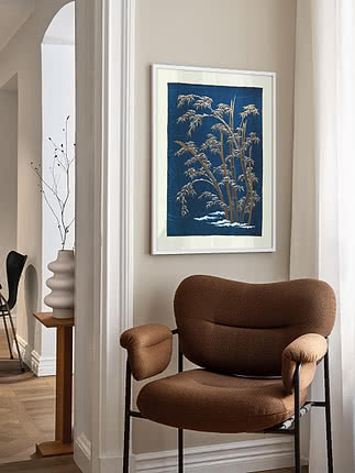 Plakaten Bamboo in Snow i hvid ramme på beige entrévæg, over en brun bouclé-lænestol ved en buet døråbning