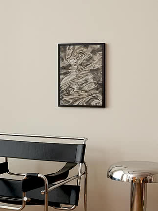 Poster Mercury im schwarzen Rahmen an beiger Wand über einem Loungesessel aus schwarzem Leder und Chrom, daneben ein Hocker aus poliertem Chrom