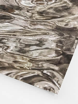 Schräge Nahaufnahme des ungerahmten Drucks mit den reflektierenden Falten, den beinahe weißen Lichtern und der Körnung über der metallischen Oberfläche