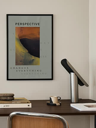 Perspective poster in a black frame on a cream wall above a walnut desk with a black and chrome lamp and books