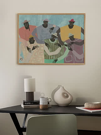 Plakaten Group Chat i egeramme på en lys væg over et sort skrivebord med en keramisk bordlampe, en stak bøger, en cremefarvet buget vase og et flettet fad, ved siden af en salviegrøn stol