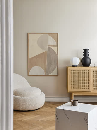 Plakat Textured Harmony w dębowej ramie na jasnej ścianie obok kremowego fotela z bouclé, z dębową komodą z plecionką, na której stoi biała kulista lampa i czarny żłobiony wazon