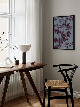 Botanical Shadows I poster in a black frame on a greige wall beside a dark wood desk with a white hemisphere lamp, a book and a brass dish, next to a black wishbone chair