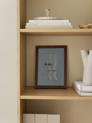 Poster Wavy Reflections II im dunklen Holzrahmen, auf einem Eichenregal stehend, neben einer weißen skulpturalen Vase und Büchern, mit einer gepunkteten Keramikfigur im Regal darüber