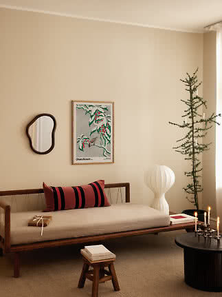 Przytulny salon z drewnianą leżanką, czerwoną poduszką w paski, lampą, choinką i świecami