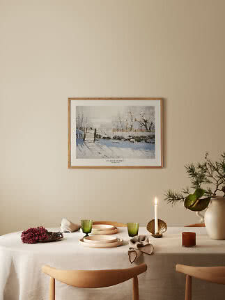 Affiche hivernale encadrée de Claude Monet au-dessus d'une table dressée avec bougie et verres verts