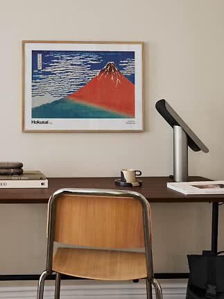 Indrammet Hokusai-plakat med rødt bjerg over skrivebord i træ