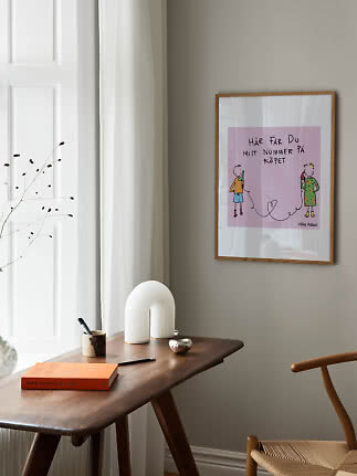 Indrammet lyserød plakat med illustration hænger over et træbord i et lyst hjørne