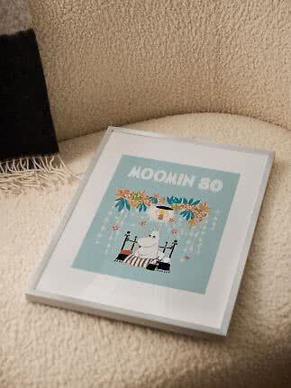 Framed Moomin print with light blue artwork resting on a cream teddy armchair