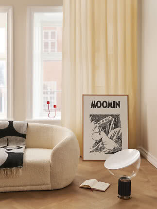 Lys stue med cremefarvet lænestol, gul gardin og Moomin-plakat op ad væggen.