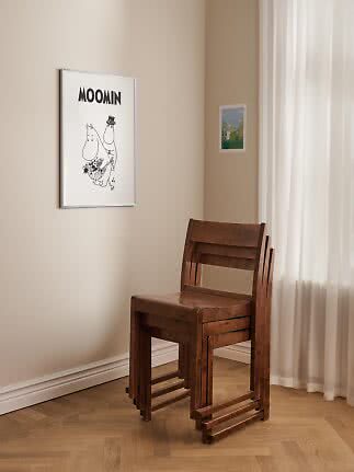 Tre stablede træstole ved beige væg med Moomin-plakat og lyse gardiner