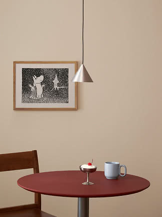 Suspension conique argentée au-dessus d’une table rouge avec mug bleu, dessert et affiche encadrée
