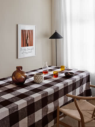 Spisebord med brunternet dug, glas, vase og sort gulvlampe ved lyst vindue