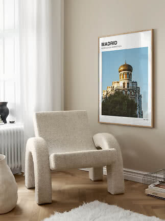 Gerahmtes Madrid-Poster mit Gebäude und goldener Kuppel an beiger Wand neben cremefarbenem Sessel
