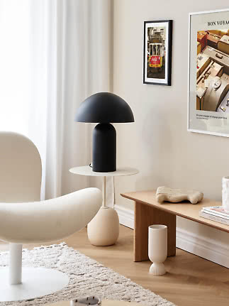Sort bordlampe med kuppelformet skærm på rundt hvidt sidebord i lys stue