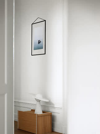 White table lamp with round shade on wooden cabinet by a white wall with framed picture