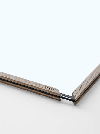Close-up of MOEBE light wood frame with acrylic panel and black rubber band at the corner
