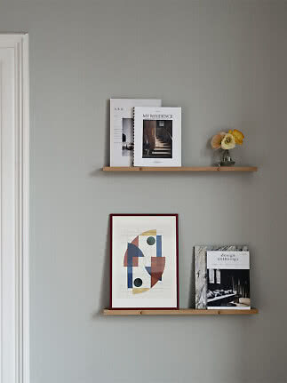 Two wooden wall shelves with magazines, framed abstract art, and a small vase of flowers.