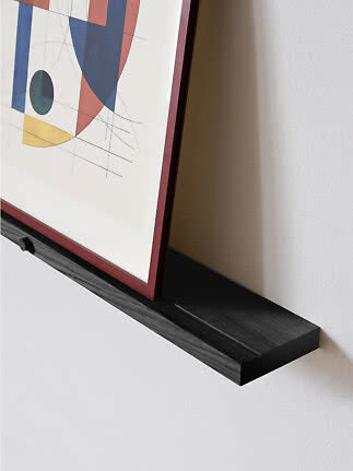 Black wooden picture ledge with framed abstract artwork on a white wall