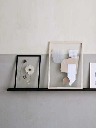 Two framed artworks on a black shelf against a light gray wall