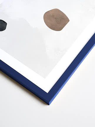 Primo piano in diagonale dell’angolo di una cornice quadrata in blu, con passepartout bianco e una stampa astratta sotto vetro