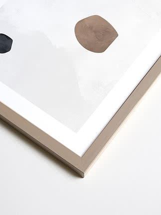 Primo piano in diagonale dell’angolo di una cornice quadrata in grigio cashmere, con passepartout bianco e una stampa astratta sotto vetro