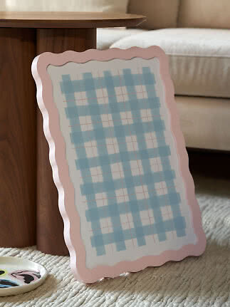 Wavy pink tray or mirror with a light blue plaid pattern, leaning against a wooden side table
