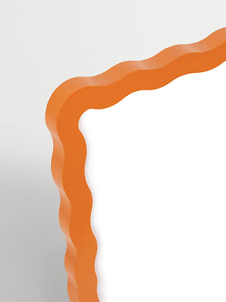 Close-up of a wavy orange mirror frame against a white background