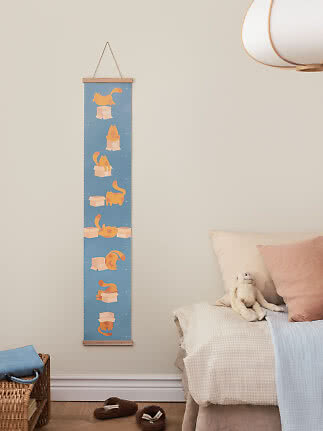 Blå højdemåler til børn med orange katte og kasser, hængende på væg ved en seng