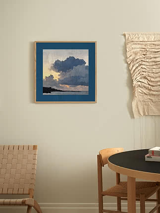 Stampa di nuvole e mare in passepartout blu e cornice in rovere accanto a un arazzo intrecciato, sopra un tavolo da pranzo