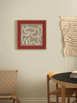 Disegno a tratto di un gatto in passepartout rosso e cornice in rovere accanto a un arazzo intrecciato, sopra un tavolo da pranzo