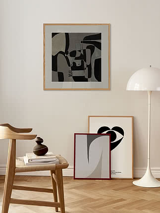 Quadro astratto in bianco e nero con passepartout grigio cashmere e cornice in rovere, sopra uno sgabello di legno e una piantana