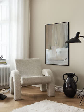 Abstrakt Sand and Sky-plakat i sort ramme over lys loungestol i roligt, beige rum