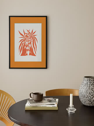 Framed orange abstract art print on a beige wall above a black table