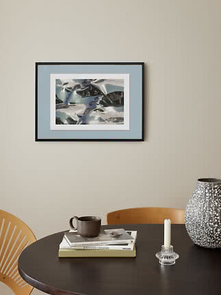 Framed abstract art print with blue and silver shapes on a beige wall above a round table