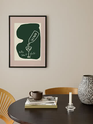 Framed abstract poster on a wall above a table with books, mug, candle holder and large vase