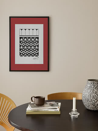 Framed black and white graphic print with red mat on beige wall above a round table