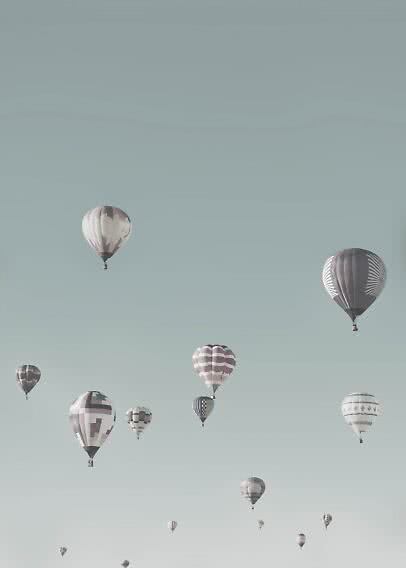 Several hot air balloons floating in a pale blue sky