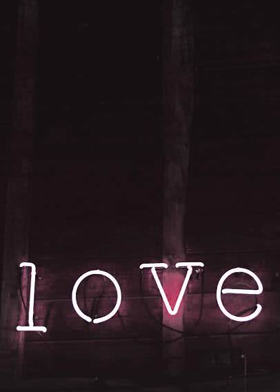 Insegna al neon rosa con la scritta "love" su una parete di legno scura