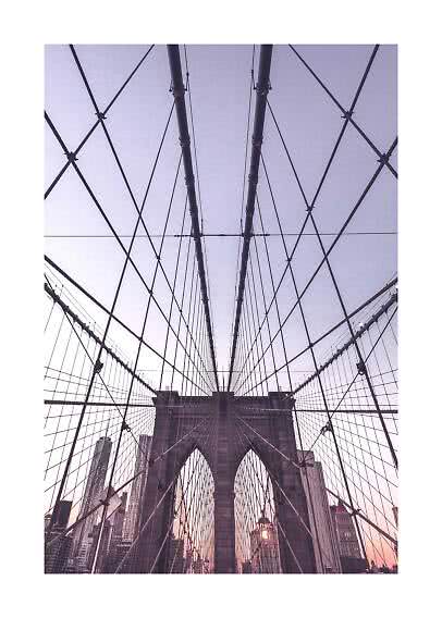 Udsigt op mod Brooklyn Bridge med krydsende kabler og bybygninger i solnedgang
