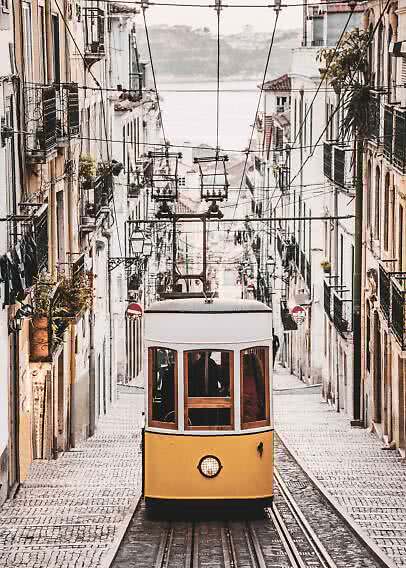 Yellow tram on a steep cobblestone street between narrow buildings and overhead wires
