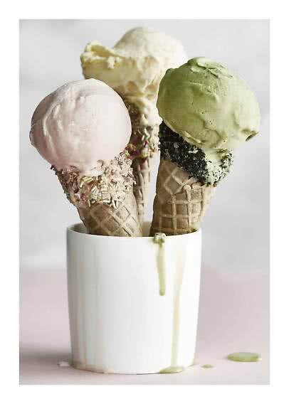 Tre coni gelato con gusti e decorazioni diverse in una tazza bianca, con gelato che si scioglie.
