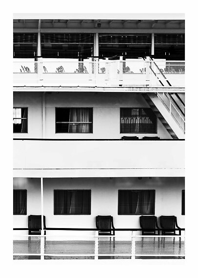 Black-and-white photo of motel walkway with balconies, windows, chairs, and exterior stairs