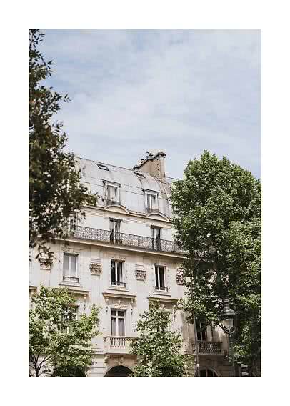 Elegantes Stadthaus mit Mansarddach, Balkonen und grünen Bäumen unter blauem Himmel