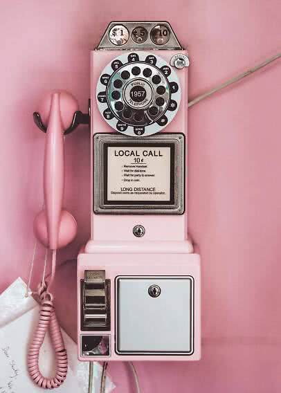 Telefono pubblico rétro rosa con disco combinatore e cornetta su parete rosa