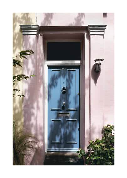 Blue front door in a pink facade with wall light, plants, and leaf shadows