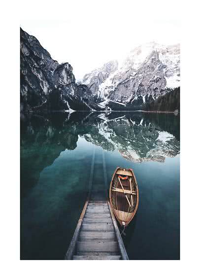 Wooden boat by a small dock on a calm mountain lake with reflected snowy peaks