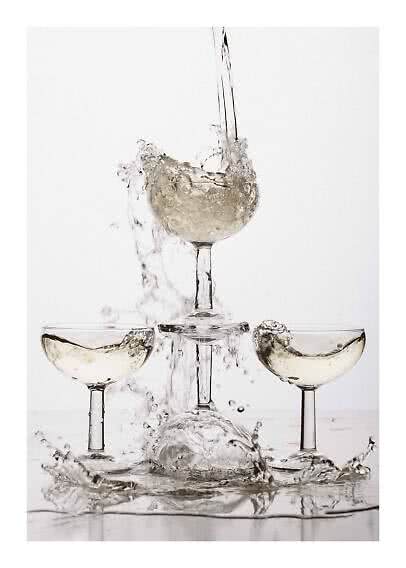 Tre coppe da champagne con vino frizzante chiaro e schizzi d'acqua su sfondo bianco